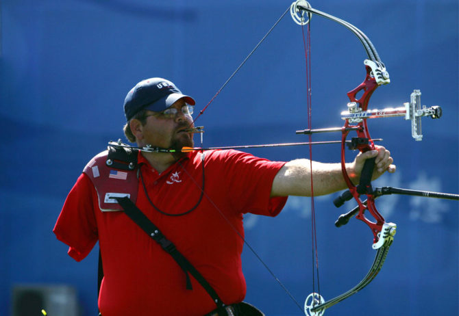 Eric Bennett a Paralympian in archery. Image of Eric lining up a shot with his bow and arrow.