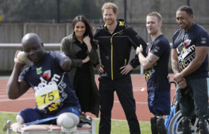 Prince Harry and Duchess Meghan stand with two men as they watch a 3rd man ready to throw for the shot put.