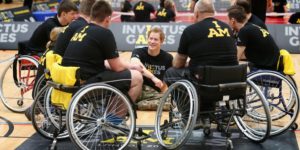 Prince Harry talking to a group of men in wheelchairs with their backs to the camera.