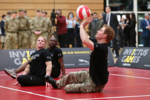 Prince Harry playing sitting volleyball as two fellow competitors look on.