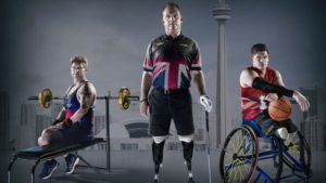 3 individuals from left to right: sitting on a workout bench facing the left, a man standing in the middle holding a golf club, and on the right an individual in a wheelchair holding a basketball looking to the right.