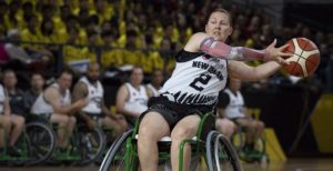 A woman playing wheelchair basketball, looking like she is catching the basketball on the right side of the image.