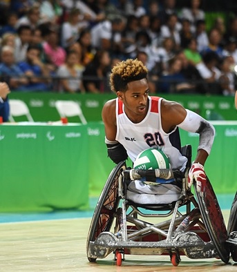 Joshua Brewer a Paralympic wheelchair rugby player. Moving down a court in his wheelchair playing rugby in a white jersey.