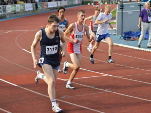 A group of young male runners competing in a race as they run around a track.