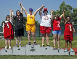 A group of individuals outside on a podium ranging from places 1st to 6th all with their arms raised in the air.