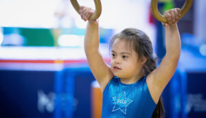 A young female gymnast holding onto the rings preparing to compete.