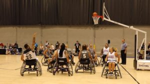A team of wheelchair basketball players all gathered around the hoop as the ball goes into the net.